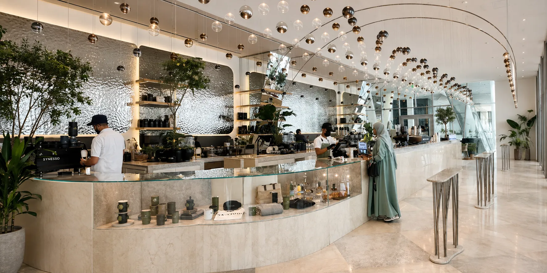 Wide view of a café interior with a suspended arced light installation, service counter, and staff serving a customer, representative of the hospitality concept underwritten in this model